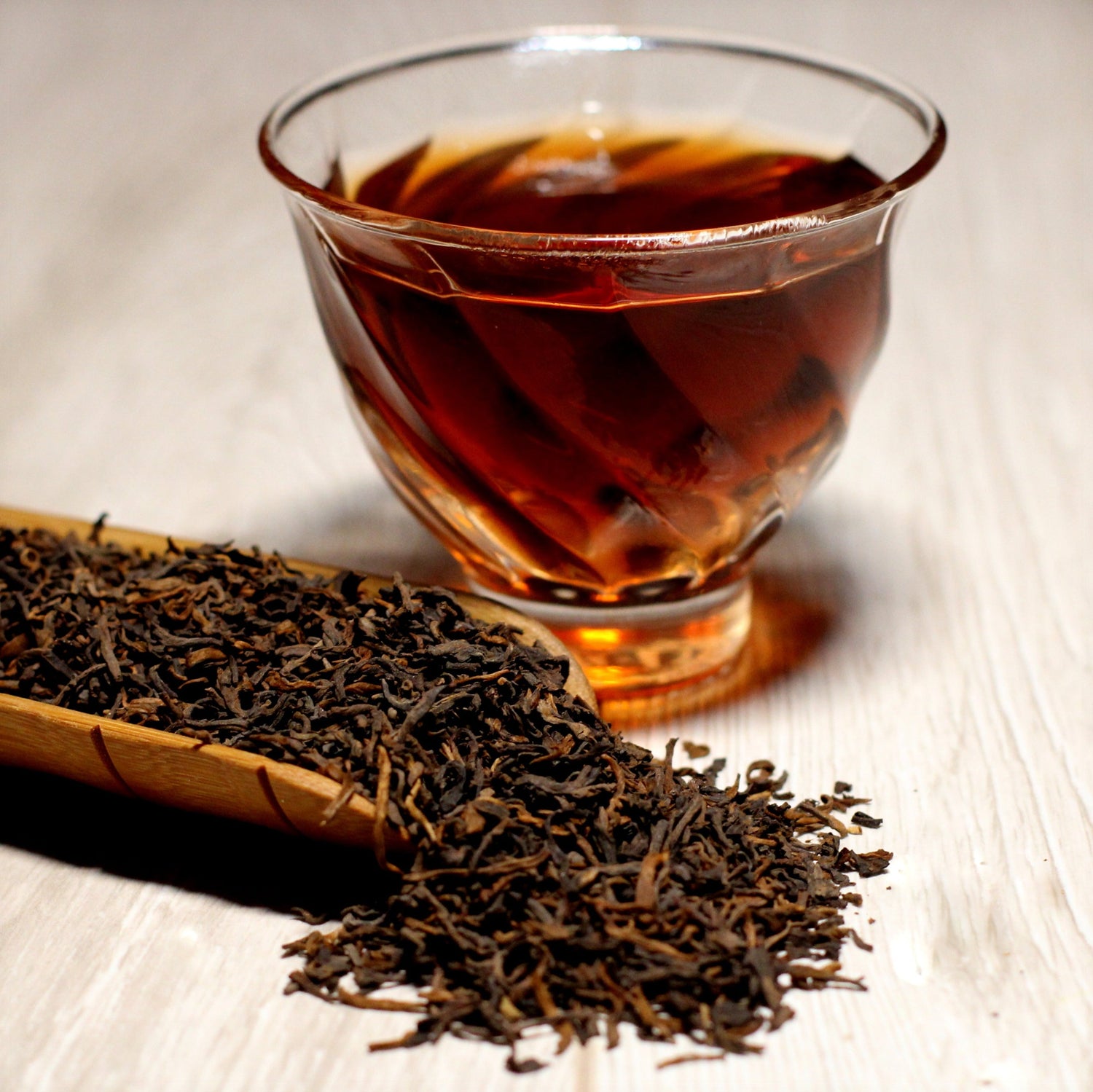 Amber black tea in a glass cup with loose leaf tea beside it